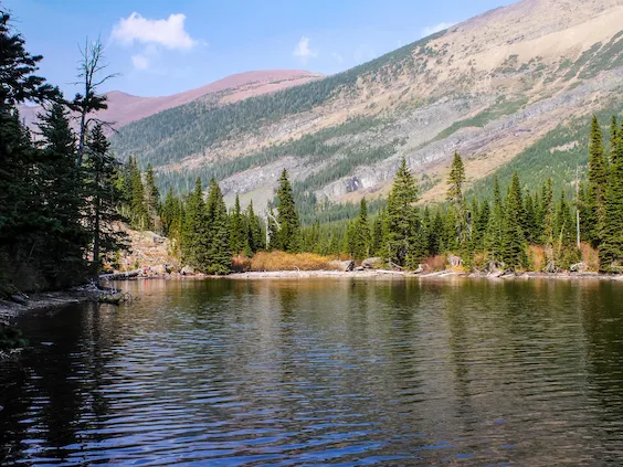 Image of the Rowe Lakes with emerald green waters and calm reflective surface reflecting the background pine forest and rocky mountain vistas.