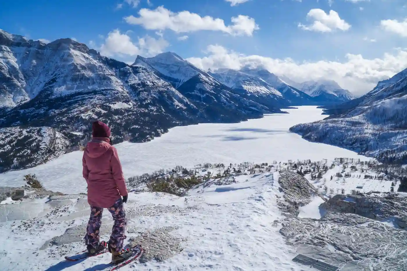Image of a in winter equipment and coat wearing snowshoes and overlooking Waterton National Park Main Lake and the Townsite from a hiking trail on a mountain